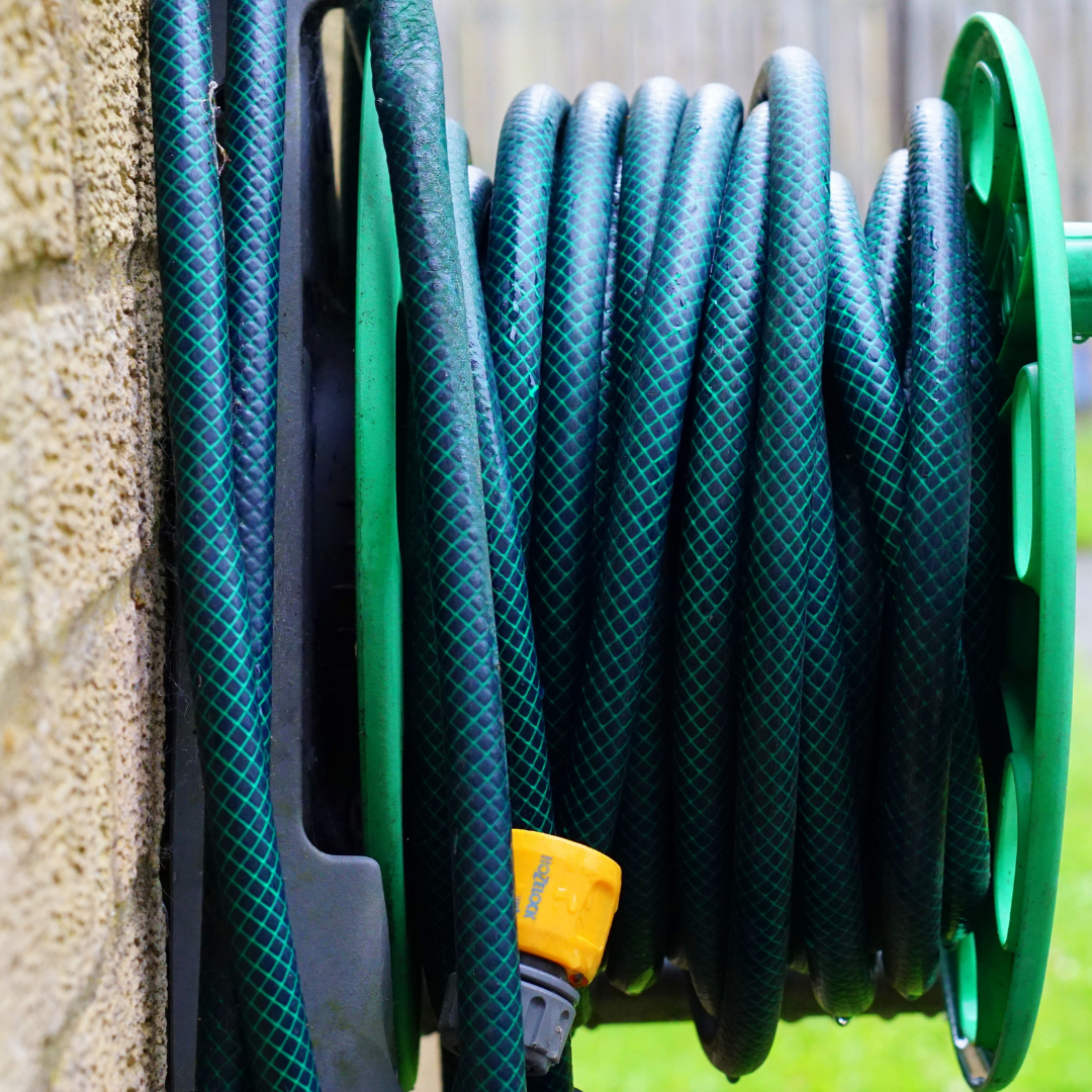 A green garden hose coiled on a wall-mounted reel, with a yellow connector visible.