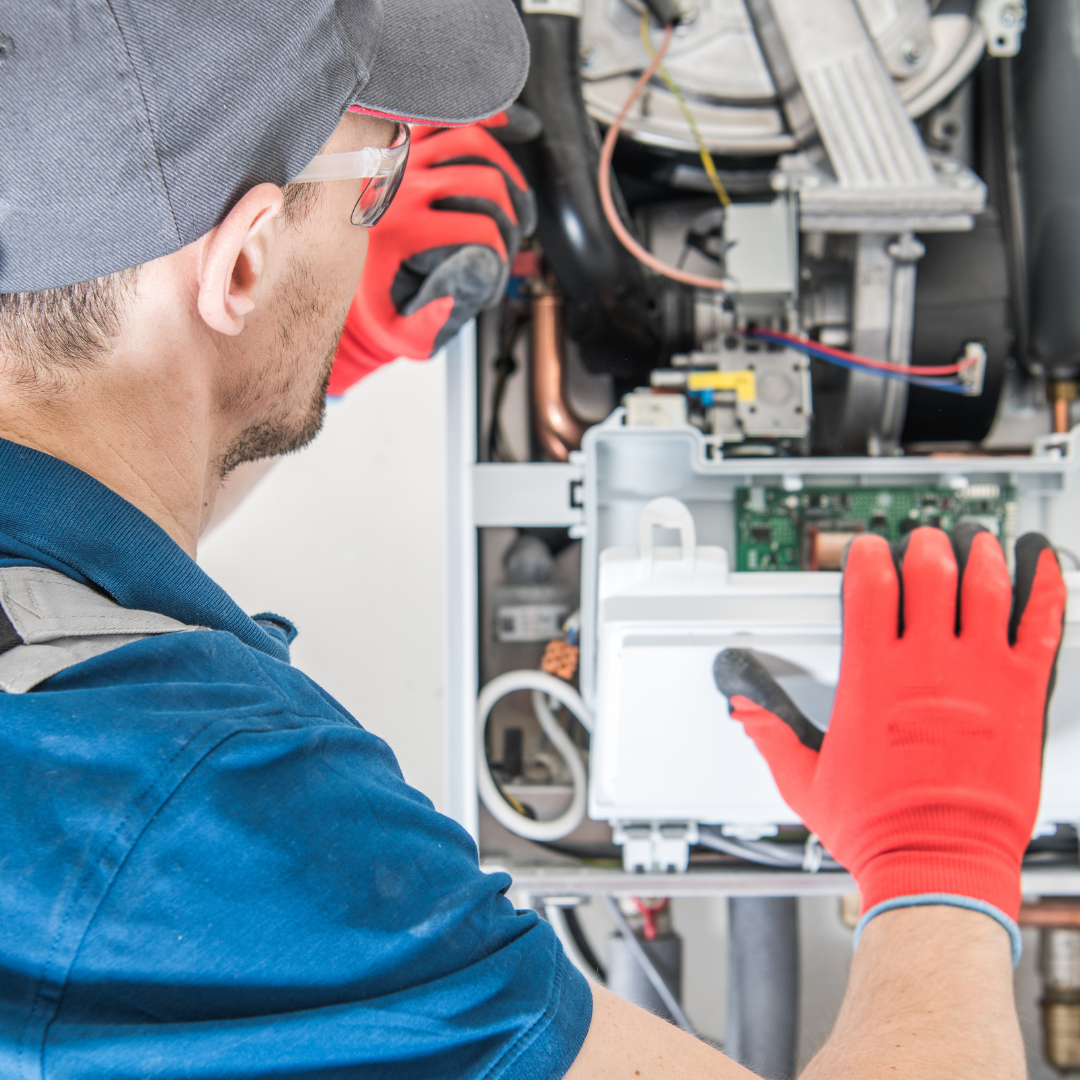 A technician in a blue shirt and red gloves is working on a machine, inspecting internal components.